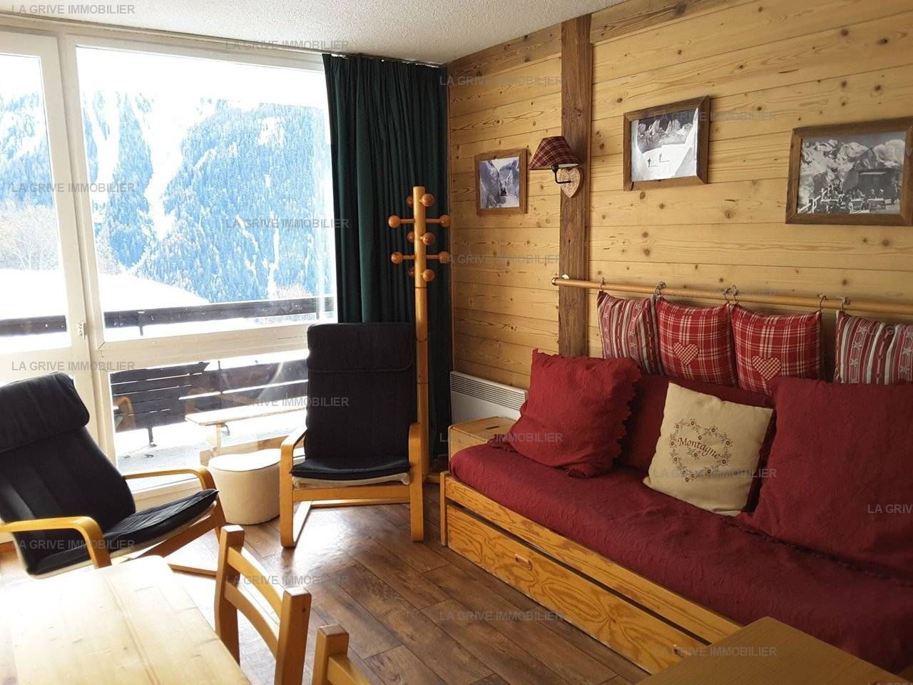 Une pièce chaleureuse avec un plancher en bois, un canapé rouge orné de coussins en forme de cœur, un fauteuil noir et une table en bois.