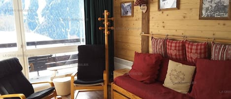 Une pièce chaleureuse avec un plancher en bois, un canapé rouge orné de coussins en forme de cœur, un fauteuil noir et une table en bois.
