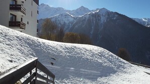 Eine verschneite Berglandschaft mit einem Gebäude, das Balkone und eine hölzerne Bank im Vordergrund zeigt.