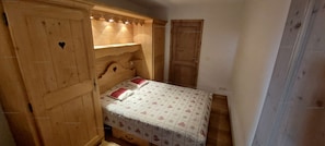 Une petite chambre à coucher accueillante, avec une tête de lit en bois, un lit simple avec une literie à motifs et une armoire ornée de découpes en forme de cœur.