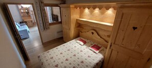 Ein Schlafzimmer mit einem hölzernen Kopfteil, einem Bett mit gemusterten Bettbezügen und einem kleinen Fenster.