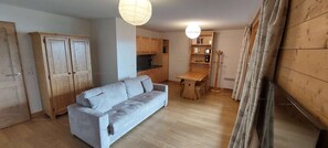 A compact living space with a sofa, wooden cabinets, a kitchenette, and a dining table.