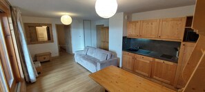 Ein gemütlicher Wohnbereich mit Sofa, Holzschränken, einer Küchenzeile und einem Esstisch.