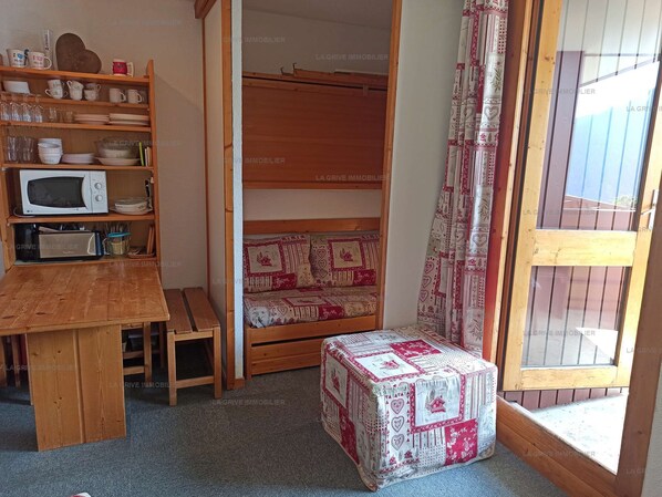 A compact room with a wooden table, a microwave, a bench, and a small stool.