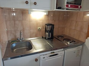Una cocina compacta con un lavabo, una cafetera, un lavavajillas y una estufa.