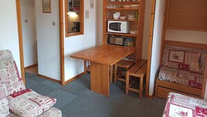 A compact living space with a wooden table and benches, a microwave, and a shelf with kitchenware. - Paradiski closed to the slopes vallandry (LANDRY)