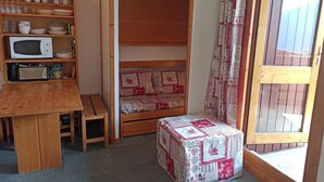 A compact room with a wooden table, a microwave, a bench, and a bed with patterned bedding. - Paradiski closed to the slopes vallandry (LANDRY)