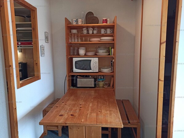 Una cocina compacta con una mesa de madera, un microondas y estantes con vajilla y cristalería.