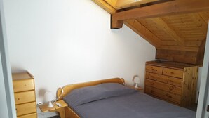 A small, single-bed room with a sloped ceiling, wooden furniture, and a simple bedside table with a lamp. - Paradiski closed to the slopes vallandry (LANDRY)