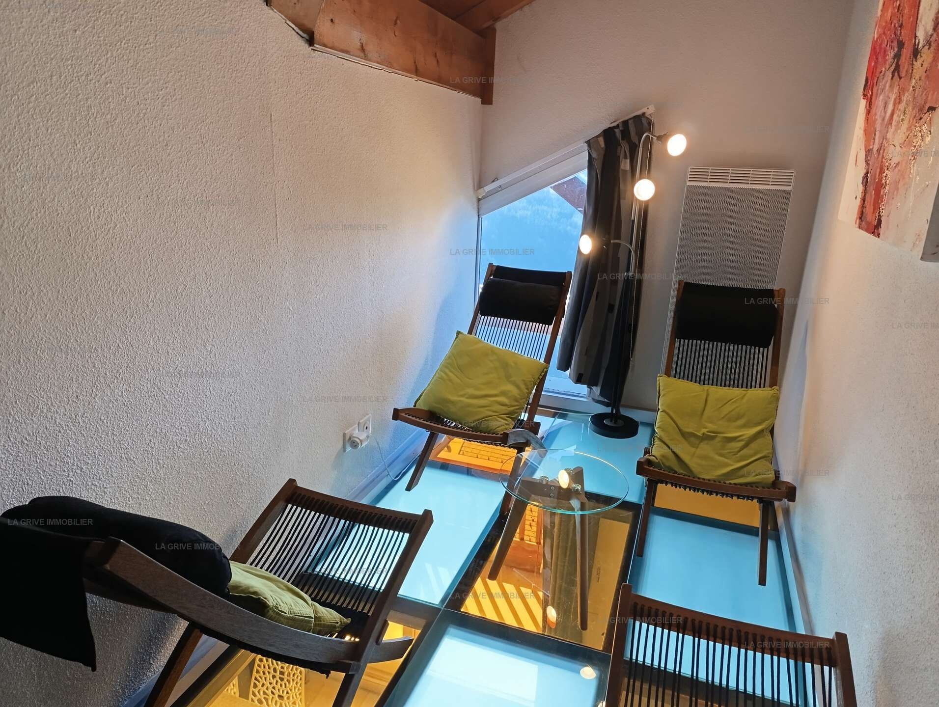 A high-ceilinged room with a glass table and two wooden chairs with cushions.