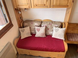 Un lit confortable avec une couverture rouge, une tête de lit en bois et des oreillers à motifs en forme de cœur.