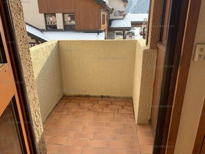 Un petit balcon fermé, doté d’un sol carrelé et offrant une vue sur un immeuble avec une enseigne.