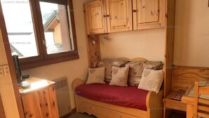 Une pièce confortable avec un lit en bois, une petite table et une fenêtre donnant sur un immeuble.