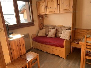 Une pièce confortable avec un lit en bois, une petite table et une fenêtre donnant sur un immeuble.
