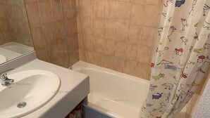 Une salle de bain avec un lavabo blanc, une baignoire et un rideau de douche à motifs animaliers.