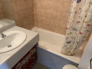 Une salle de bain avec un lavabo blanc, une baignoire et un rideau de douche à motifs animaliers.