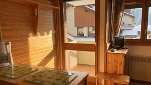 A cozy room with a wooden interior, a small wooden table with a coffee maker, a television on a wooden stand, and a view of a snowy mountain outside. - Paradiski ski in ski out vallandry (LANDRY)
