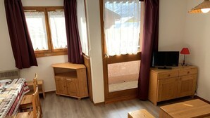 A cozy room with a wooden table, chairs, a TV, and a window with curtains.