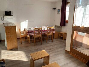A dining area with a table set for four, wooden chairs, a small wooden table, and a window with curtains.