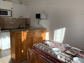 A compact kitchen with a microwave, a small refrigerator, and a wooden dining table set for two.