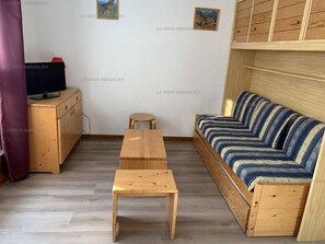 A room with a wooden sofa, a wooden table, a small stool, and a television on a wooden cabinet.