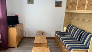 A room with a wooden sofa, a small wooden table, a wooden cabinet, and a television on a wooden dresser.