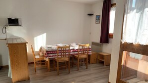 A dining area with a table set for four, wooden chairs, a small wooden table, and a microwave on a shelf.