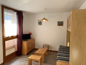 A small, cozy room with a wooden desk, a television, a bench, and a bed.