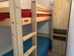 A bunk bed with a red mattress and a wooden wardrobe with a mirror.