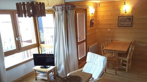 A cozy room with a television, a dining table, and a window with curtains.