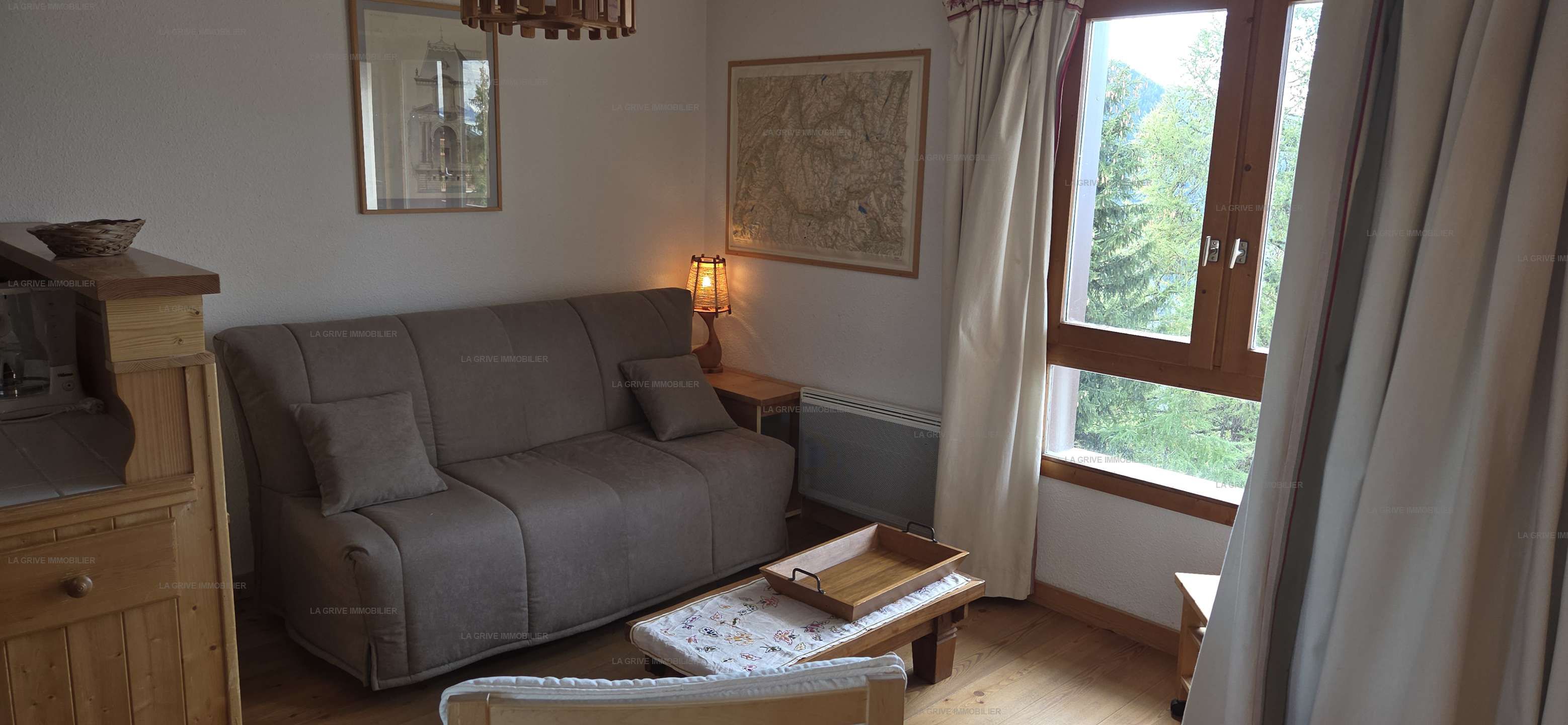 A cozy room with a sofa, a small table, a radiator, and a window with curtains.