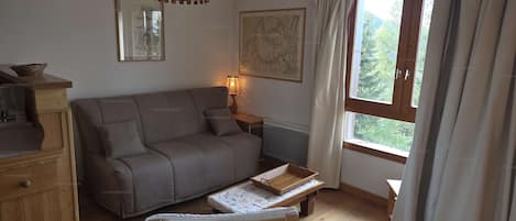 A cozy room with a sofa, a small table, a radiator, and a window with curtains.