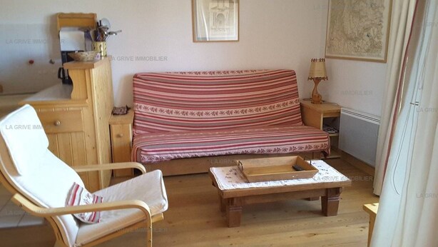 A room with a wooden floor, a striped sofa, a wooden chair, a small table, and a lamp.