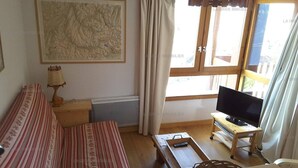 A living room with a sofa, a television on a stand, a map on the wall, and a window with curtains.