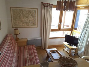 Una sala de estar con sofá, televisor sobre un mueble bajo, un mapa en la pared y una ventana con cortinas.