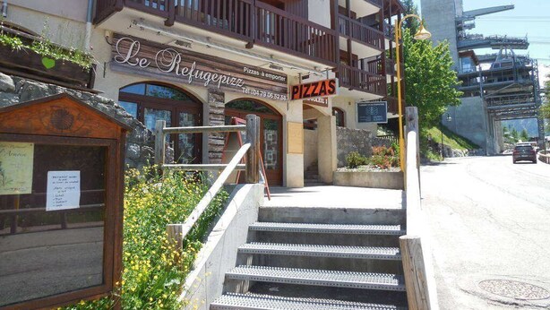 Un bâtiment avec une enseigne indiquant « Le Refuge Pizza » et un escalier menant à l’entrée.