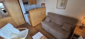 A compact living space with a wooden cabinet, a sofa, a chair, and a small kitchen area.