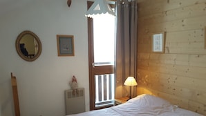 Um quarto com cabeceira de madeira, cama com roupa de cama branca, mesa de cabeceira com abajur, janela com cortinas e radiador.