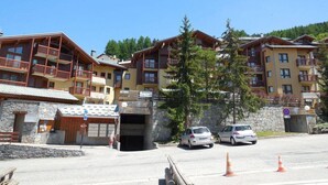 Ett hotell med flera våningar, balkonger, en fasad av sten och en parkeringsplats med bilar och trafikavspärrningskoner.