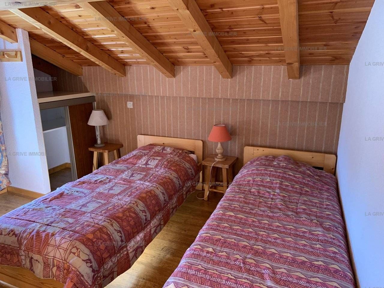 Un dormitorio con dos camas, vigas de madera en el techo, una mesita de noche con lámpara y un armario.