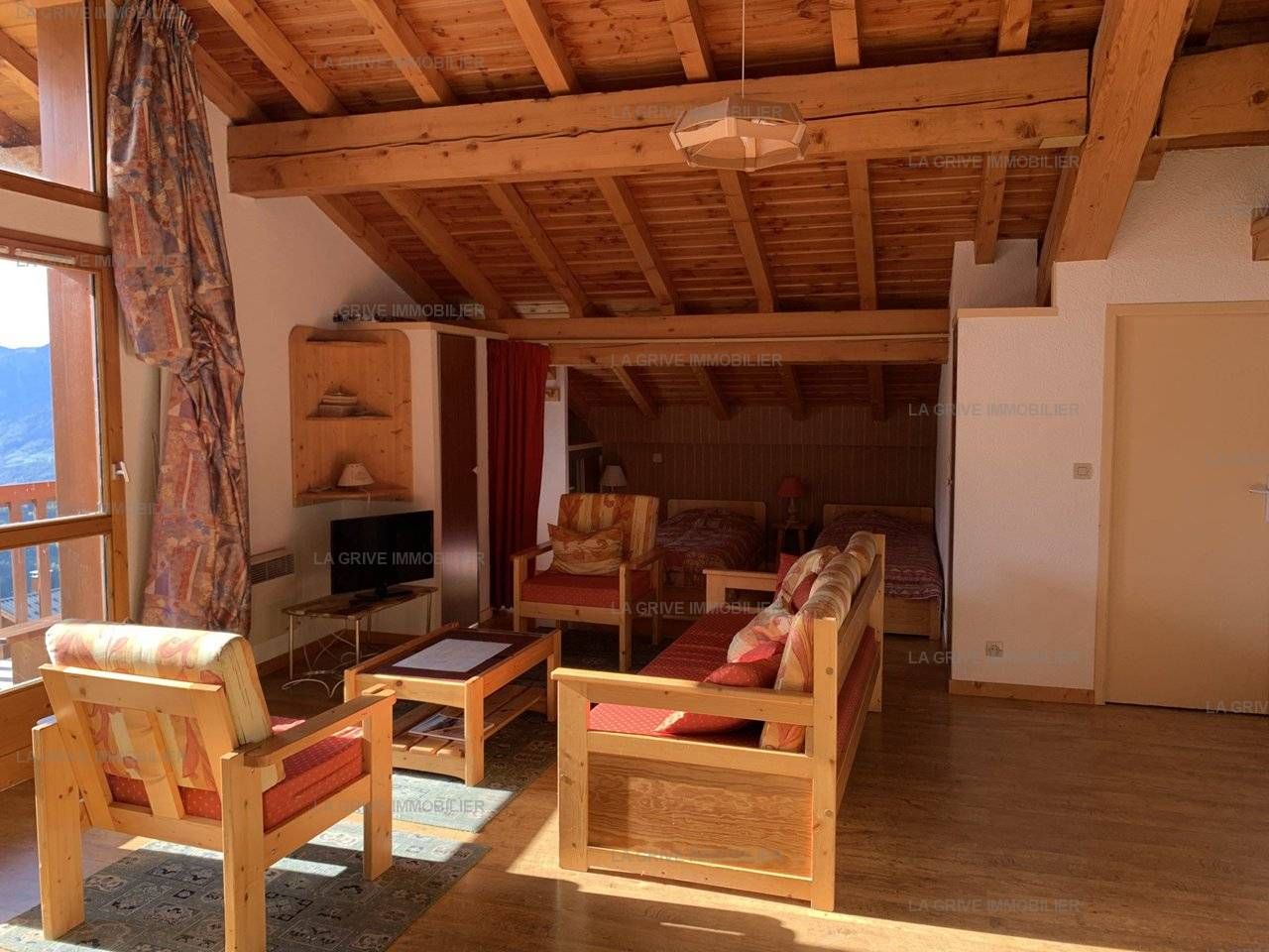 A wooden-floored living room with a television, seating area, and a view of the outdoors.