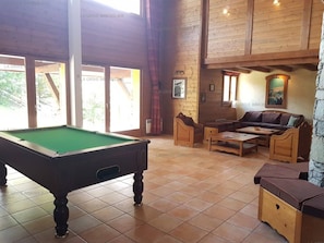 A pool table in a room with a wooden ceiling, a sofa, and a stone pillar.