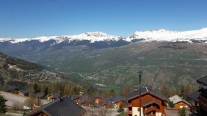 Un pueblo de montaña con picos nevados al fondo, casas con tejados inclinados y un cielo azul despejado.