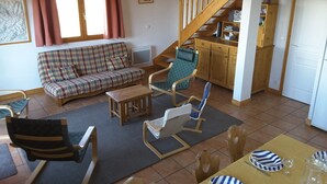 Una sala de estar acogedora con un sofá, sillas, una mesa de centro y una escalera que lleva a una cocina.