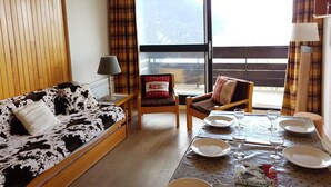A cozy living room with a sofa, chairs, a dining table set with plates and glasses, and a window with curtains.
