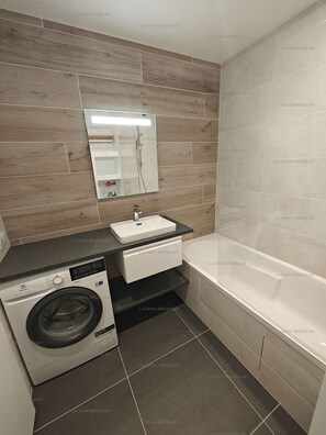 Une salle de bain moderne équipée d’un lave-linge intégré, d’un lavabo et d’une baignoire.