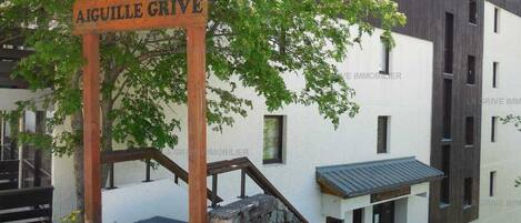 A wooden sign with the text 'AIGUILLE GRIVE' in front of a building with a modern design, a staircase, and a small porch area.