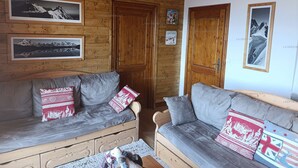 Een knus interieur van een blokhut met houten wanden en twee grijze banken met gestreepte kussens.