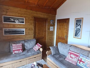 Een knus interieur van een blokhut met houten wanden en twee grijze banken met gestreepte kussens.
