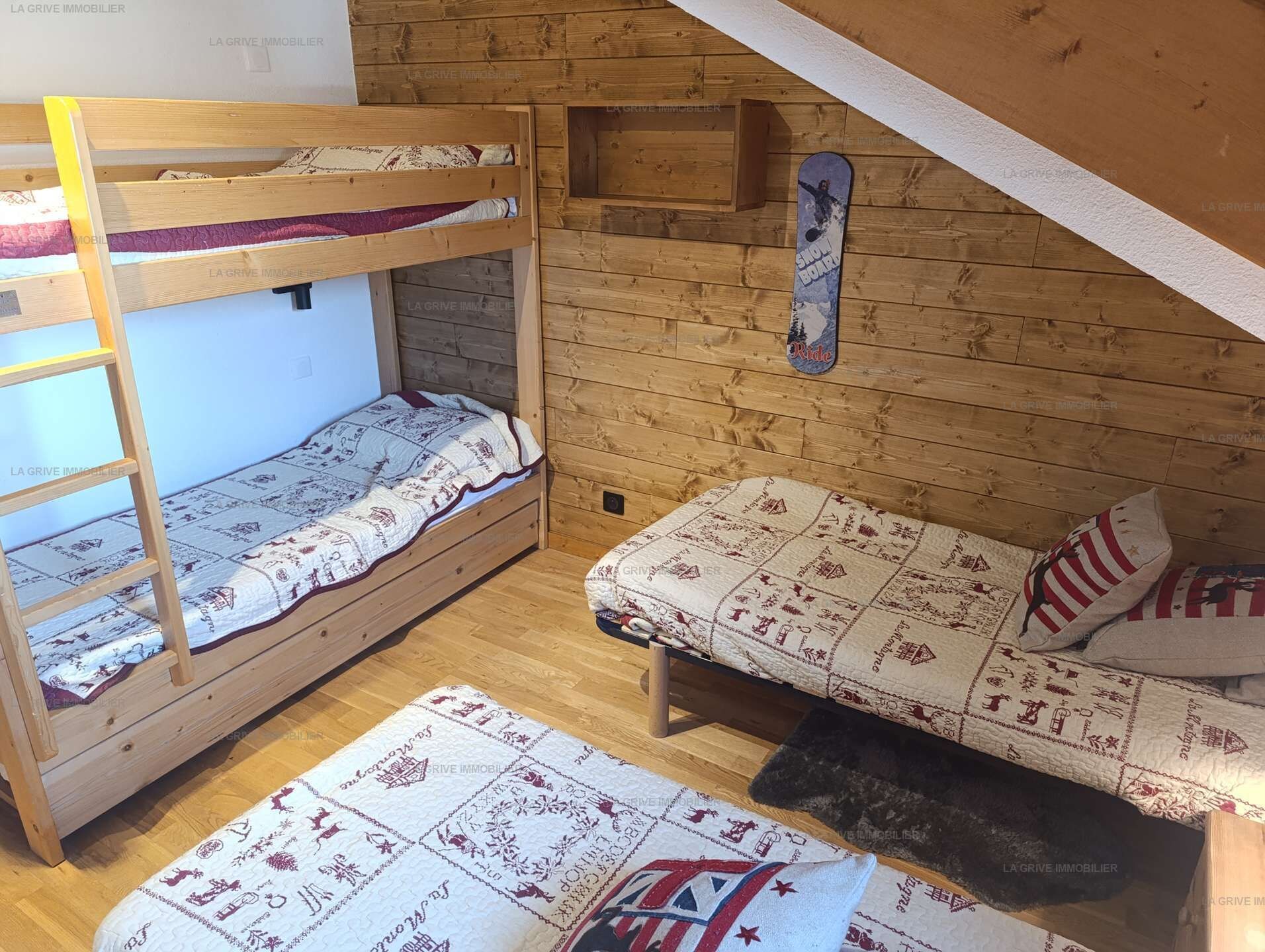 A dormitory room with bunk beds, a small shelf, and a snowboard decoration.